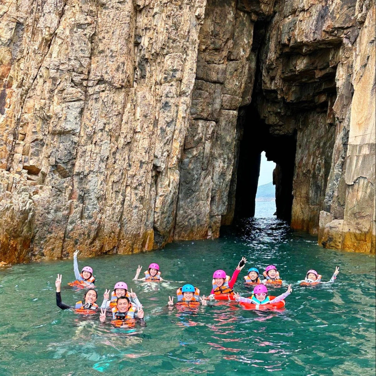 In Hong Kong Geopark, Group of people swimming in a cave entrance with rocky cliffs, experiencing coasteering with coach