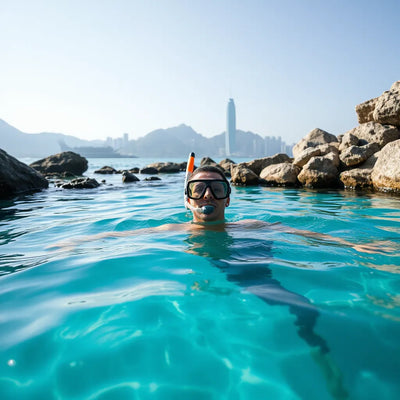 Snorkeler drifting in clear turquoise water near Hong Kong’s rocky shoreline with distant skyline