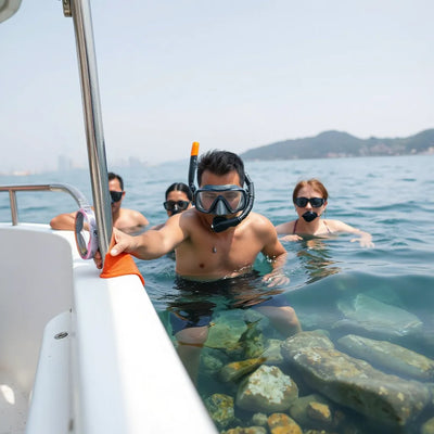 Snorkelers and a guide on a small boat near clear coastal water with Hong Kong skyline in the distance