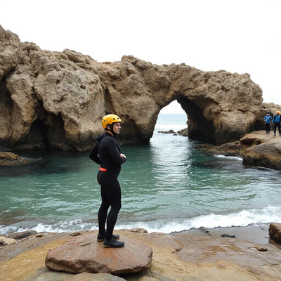 Coasteering near twin sea arches with a wetsuited group on wet limestone rocks and clear turquoise water
