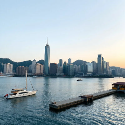 Hong Kong skyline over a calm harbor at golden hour with boats and a waterfront promenade